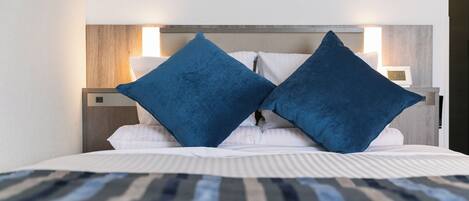 Una cama bien hecha con una colcha a rayas, dos almohadas azules y un cabecero de madera con dos lámparas de pared.