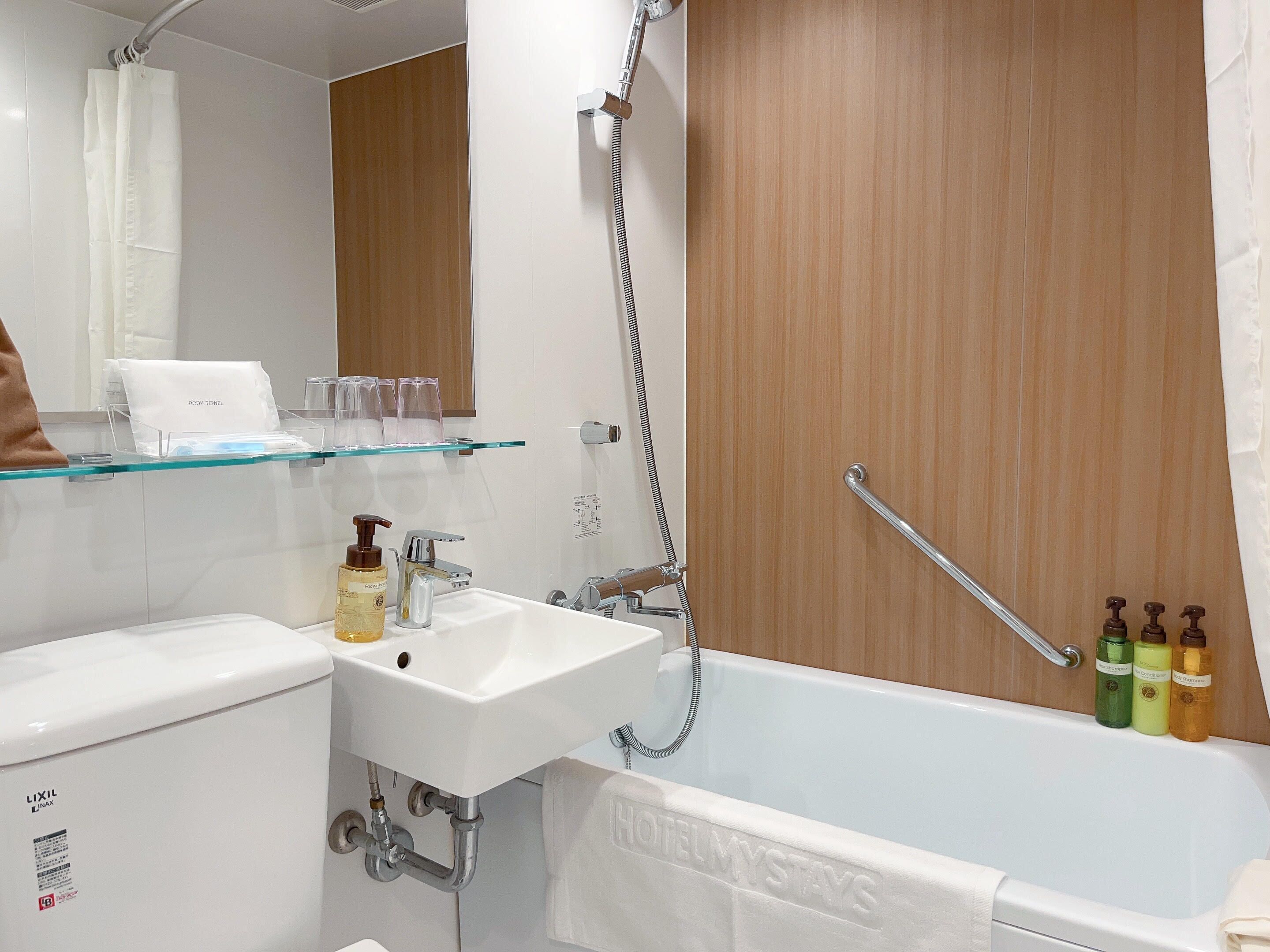 A bathroom with a white sink, a bathtub, and a shower. There are toiletries on the sink and a towel hanging on the wall.