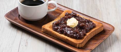 A slice of toast with jam and a pat of butter on a wooden tray, accompanied by a cup of coffee.