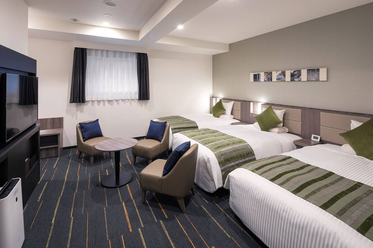 A hotel room with two beds, a TV, a desk, and a chair.