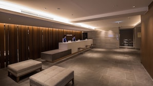 Ein moderner Hotel-Empfangsbereich mit einem Holzbüro, zwei Angestellten und einer Lounge mit Hocker.
