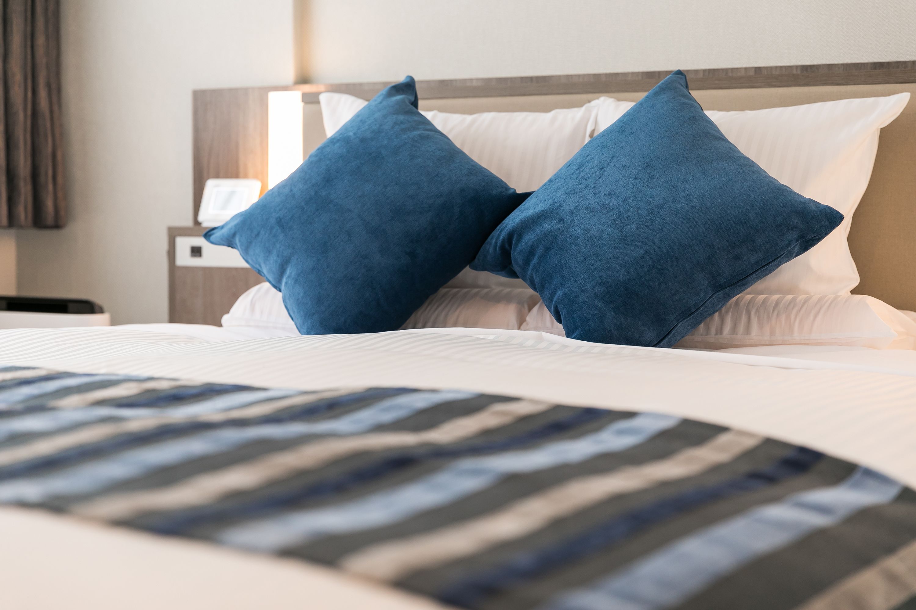 A bed with white linens and two blue pillows, a wooden headboard, and a striped blanket.