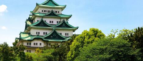 A traditional multi-tiered castle with green roofs, surrounded by lush greenery.