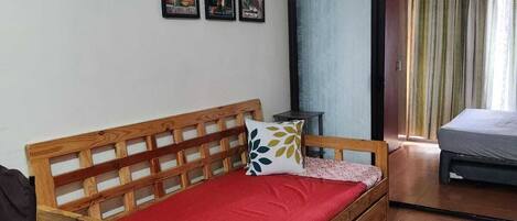 A wooden bed with a red mattress and a wooden headboard in a room with a tiled floor, a ceiling fan, and three framed pictures on the wall.