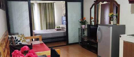 A compact living space with a bed, a dining table with chairs, a kitchenette, and a ceiling fan.