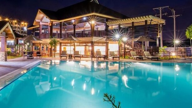A hotel with a swimming pool, outdoor seating, and a well-lit exterior at night. - 1 Bedroom Condo at One Oasis Condominuim (Cagayan de Oro)