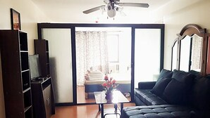 A living room with a sofa, a coffee table, and a TV on a stand. There is a sliding glass door leading to a balcony with a view of the outside. - 1 Bedroom Condo at One Oasis Condominuim (Cagayan de Oro)