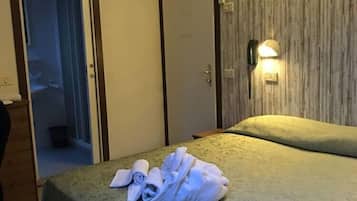 Habitación de hotel con cama, mesita de noche, armario y baño visible a través de una puerta abierta.