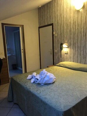 Ein Hotelzimmer mit Bett, Nachttisch, Kleiderschrank und einem durchgehenden Türbogen einsehbarer Badezimmers.