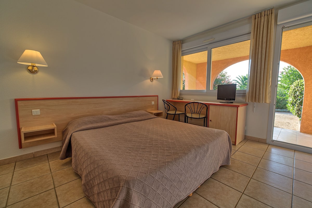 A hotel room with a large bed, a desk with a television, and a window with curtains.