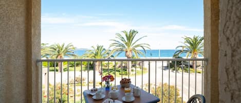 A balcony with a table set for breakfast overlooking a beach with palm trees and the ocean.