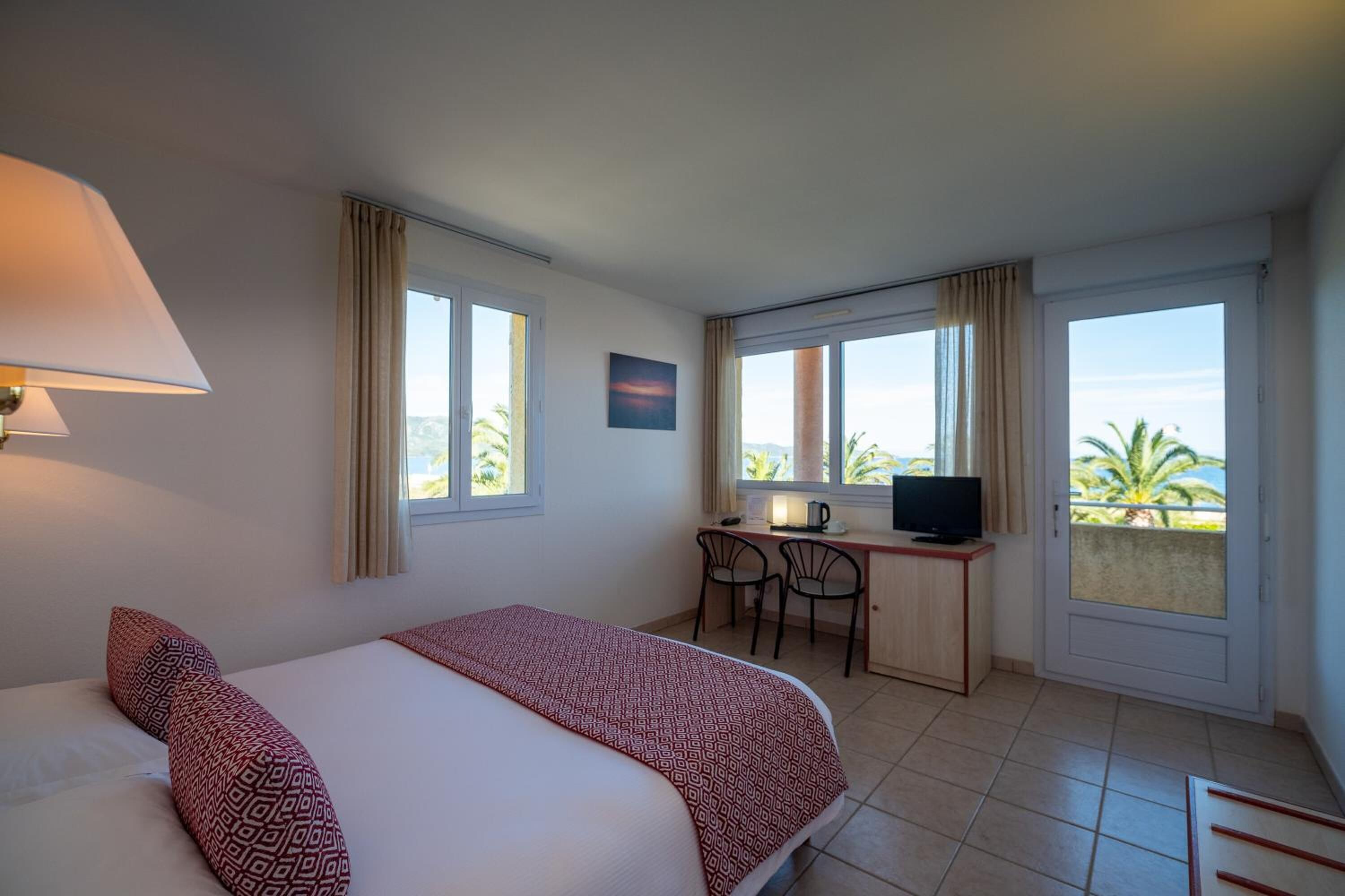 Une chambre d’hôtel avec un lit, un bureau avec une télévision et une vue sur les palmiers.