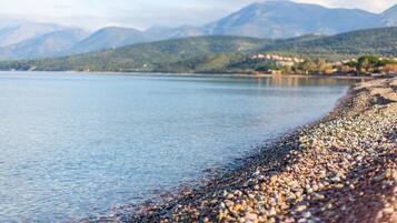 Una playa de guijarros con un lago tranquilo y montañas al fondo.