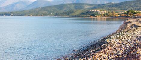 Una playa de guijarros con un lago tranquilo y montañas al fondo.