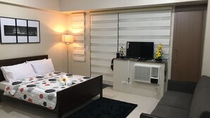Una habitación de hotel con una cama, un escritorio con computadora, un televisor y un armario.
