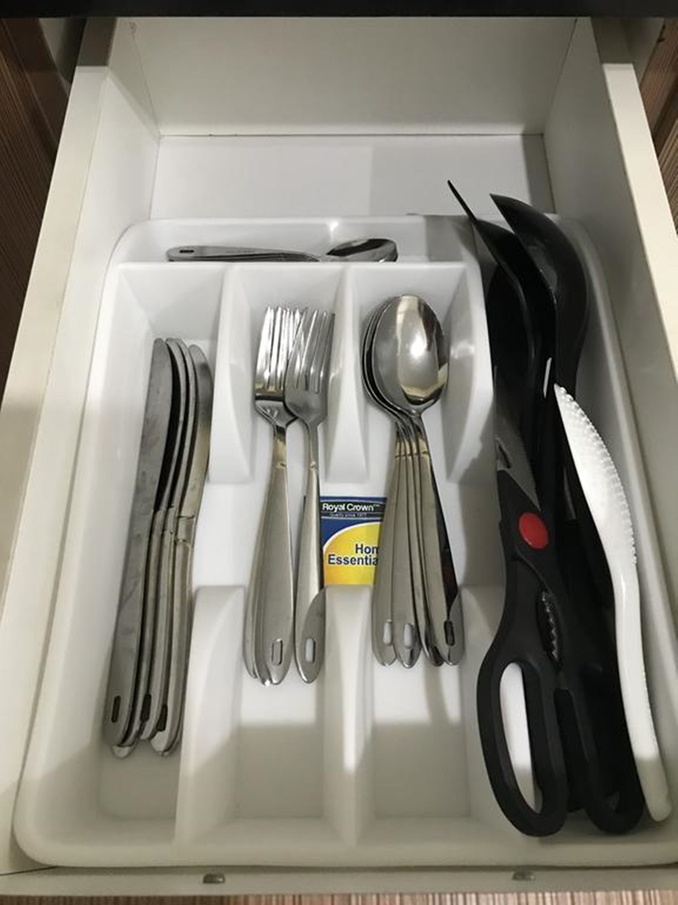 Eine Schublade mit ordentlich sortiertem Besteck, darunter Gabeln, Messer und Löffel, sowie eine Schere.