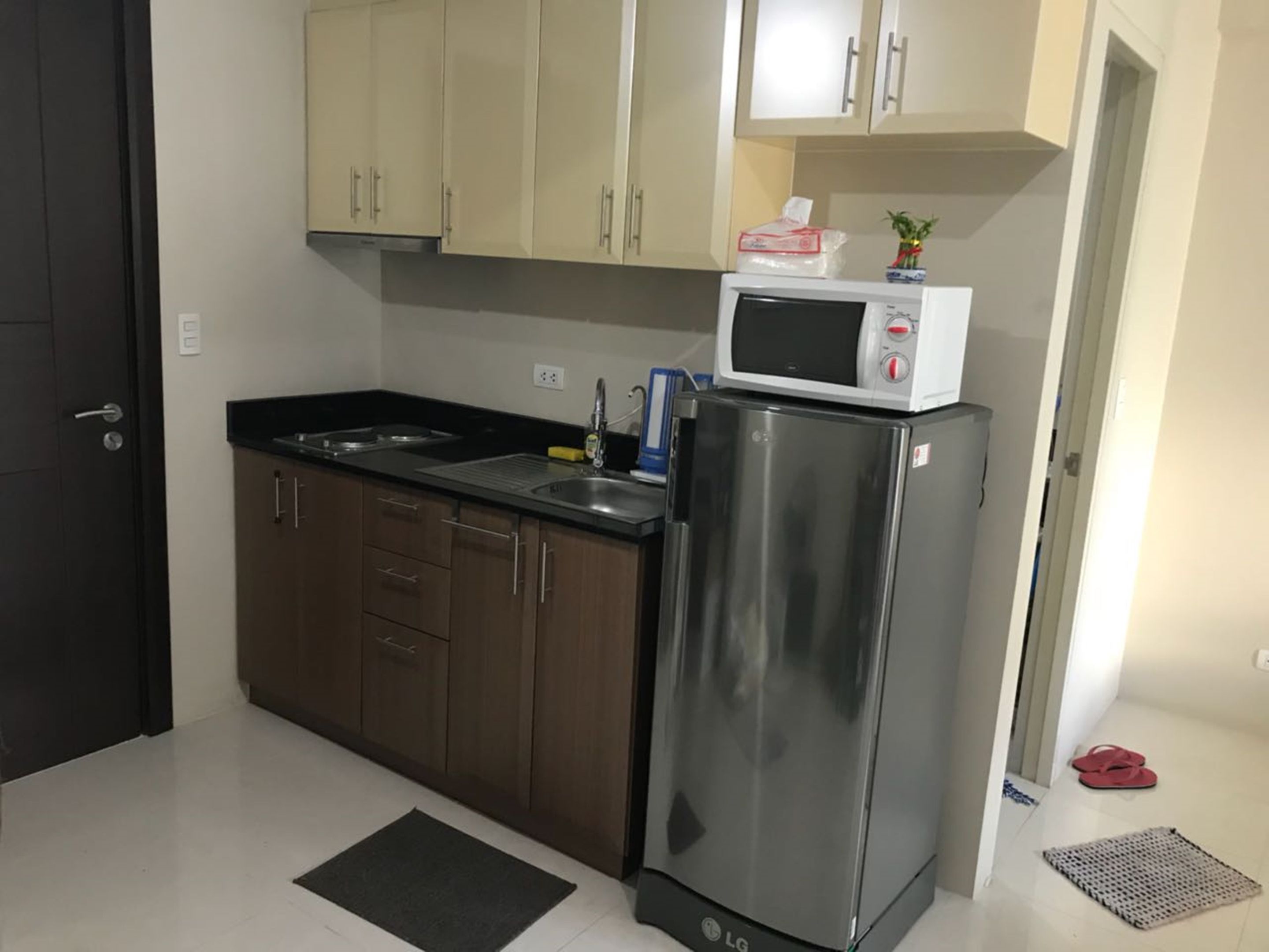 Una cocina compacta con un refrigerador de acero inoxidable, un microondas y un lavamanos.