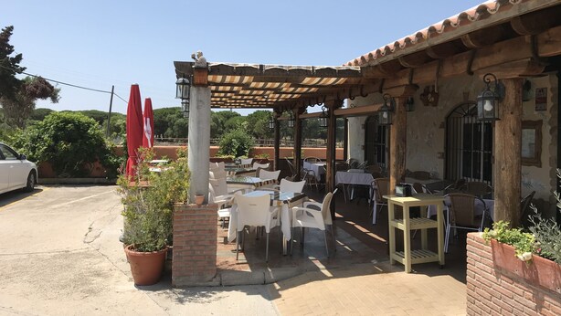 An outdoor patio with tables and chairs, a brick wall, and a car parked nearby. - Hostal Restaurante El Mero (Barbate)