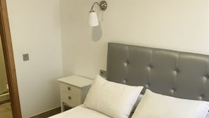 A neatly made bed with a grey headboard, white pillows, and a white bathrobe on the bed. - Hostal Restaurante El Mero (Barbate)