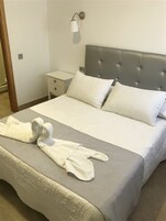 A neatly made bed with a grey headboard, white pillows, and a white bathrobe on the bed.