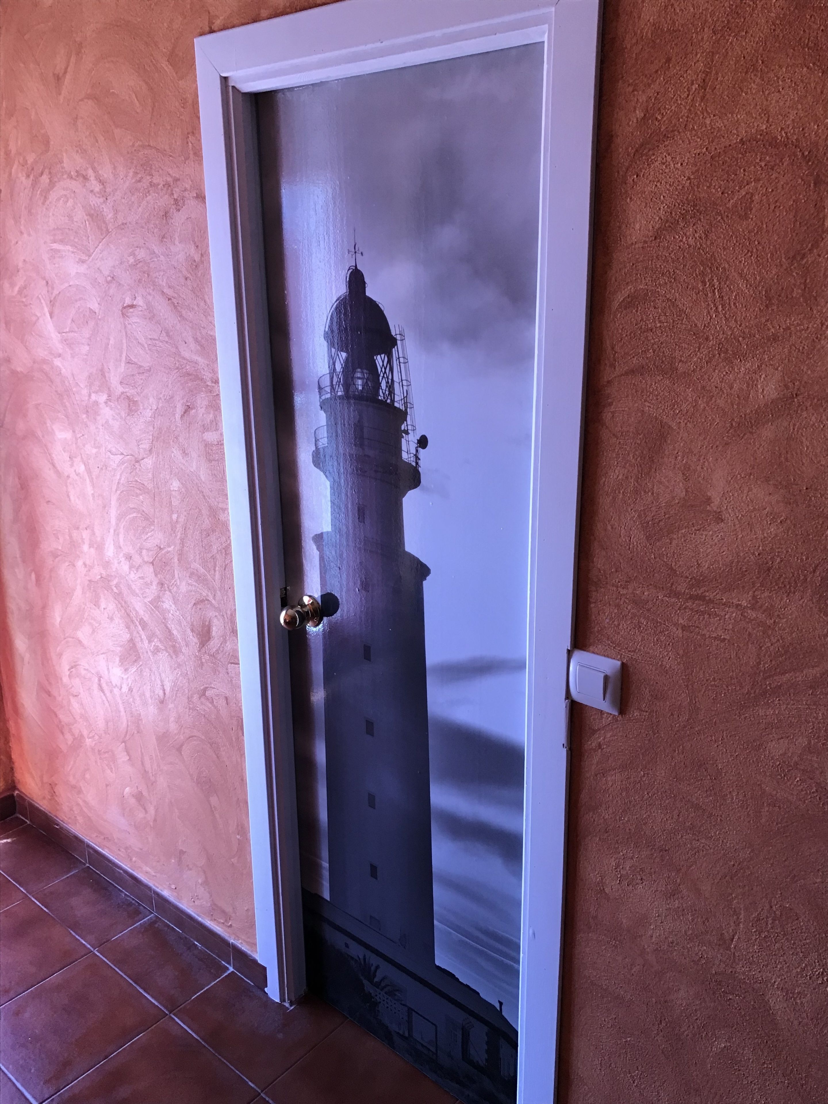 Une porte dotée d’un panneau de verre représentant la silhouette d’un phare.