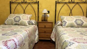 Una habitación con dos camas, cada una con un edredón estampado y almohadas a juego, una mesita de noche de madera con lámpara y suelo de baldosas.