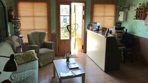 A cozy room with a wooden ceiling, a green sofa, a small table, a chair, and a desk with a computer. - Hostal Restaurante El Mero (Barbate)