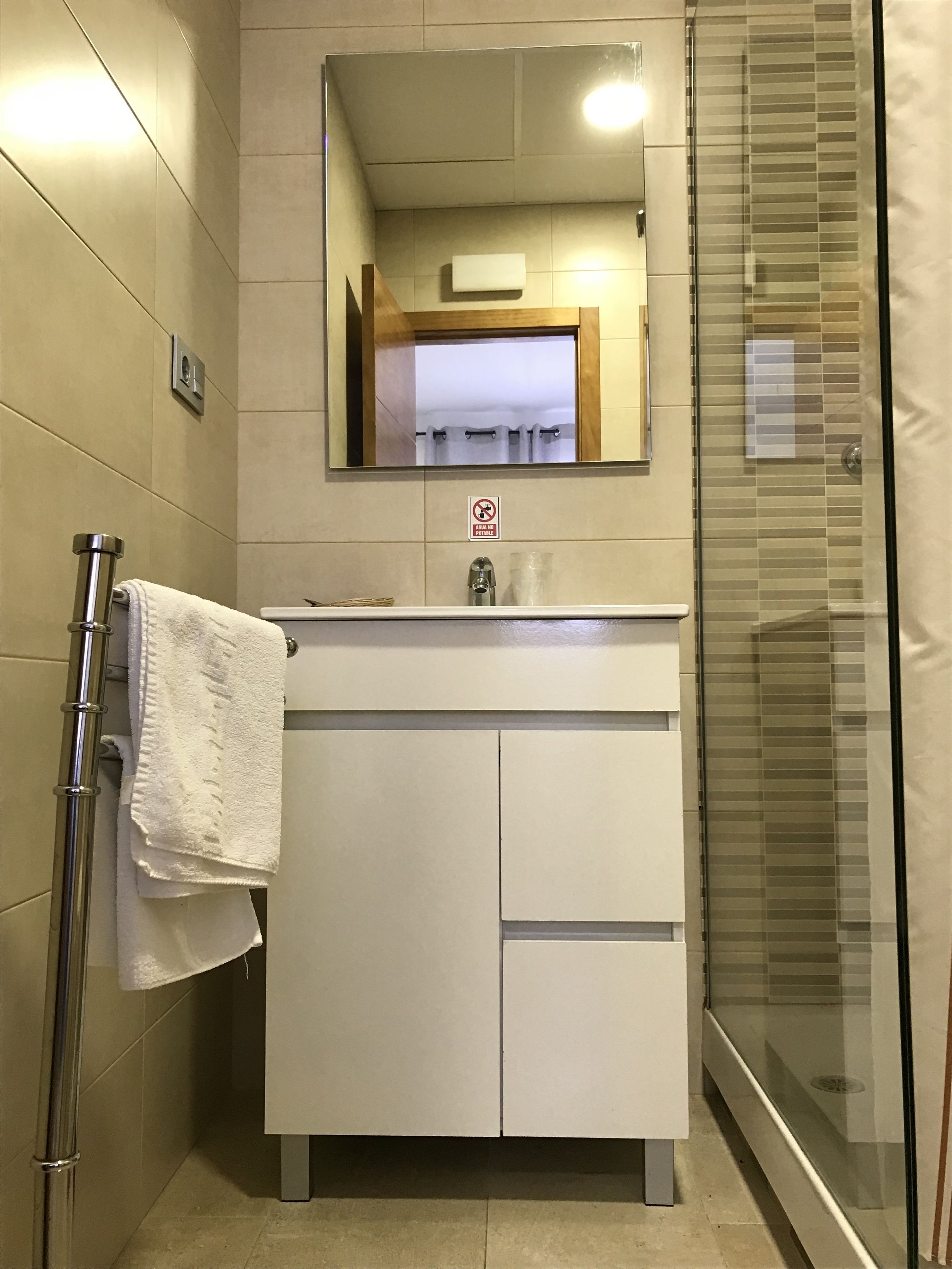 Un baño con lavamanos blanco, espejo y cabina de ducha de vidrio.