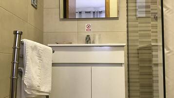 Un baño con lavamanos blanco, espejo y cabina de ducha de vidrio.