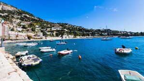 A coastal town with boats docked along the waterfront, buildings on a hillside, and a clear blue sky. - QUAI DES MARINIERES AP2015 by RIVIERA HOLIDAY HOME (Villefranche-sur-Mer)