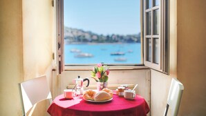 A table with breakfast items, a vase of flowers, and a view of boats on water through a window. - QUAI DES MARINIERES AP2015 by RIVIERA HOLIDAY HOME (Villefranche-sur-Mer)