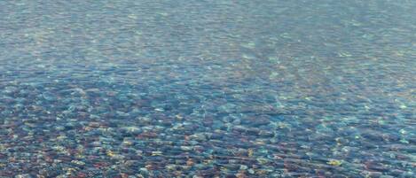 A clear view of a pebble beach with a calm sea and distant landforms.