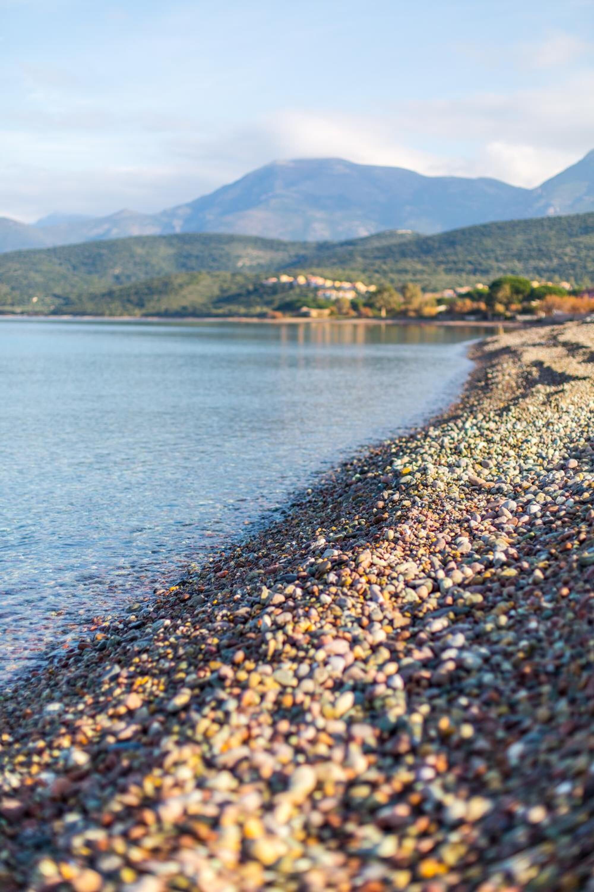 Ein Kiesstrand mit einem ruhigen See und Bergen im Hintergrund.