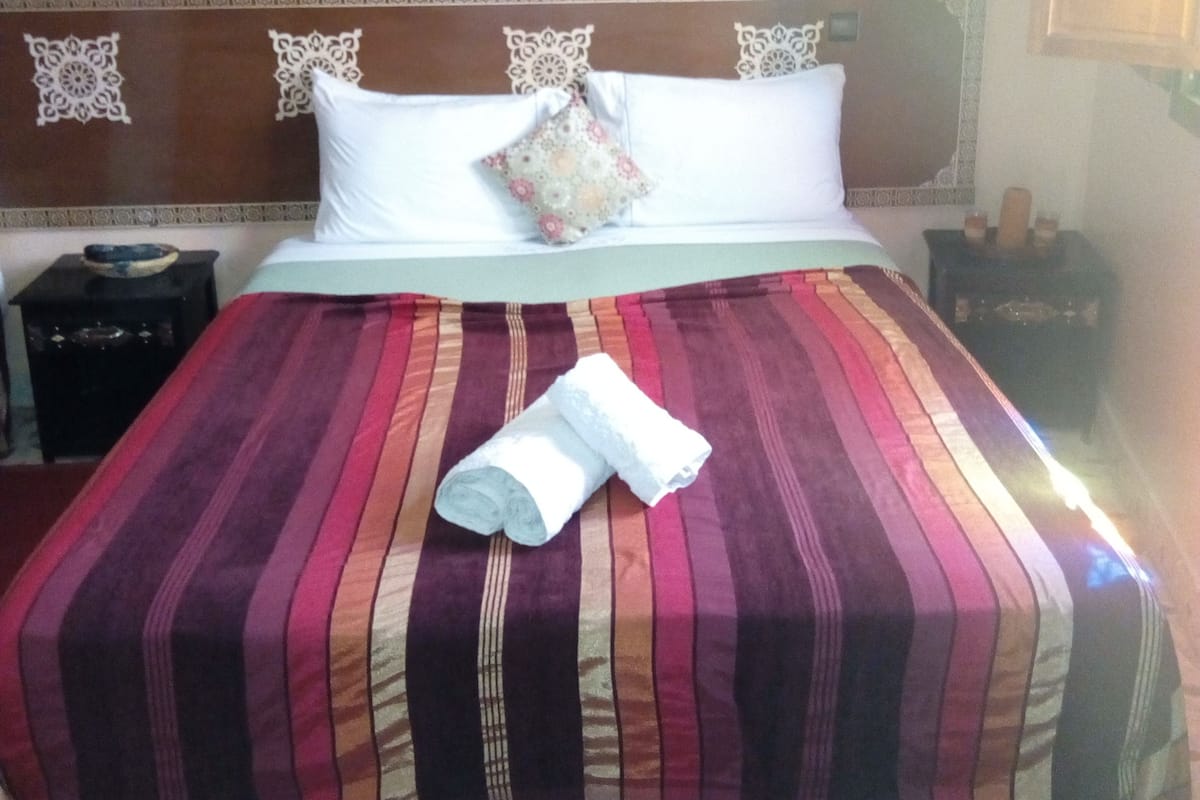 A neatly made bed with a striped bedspread, two pillows, and a rolled towel on the bed.