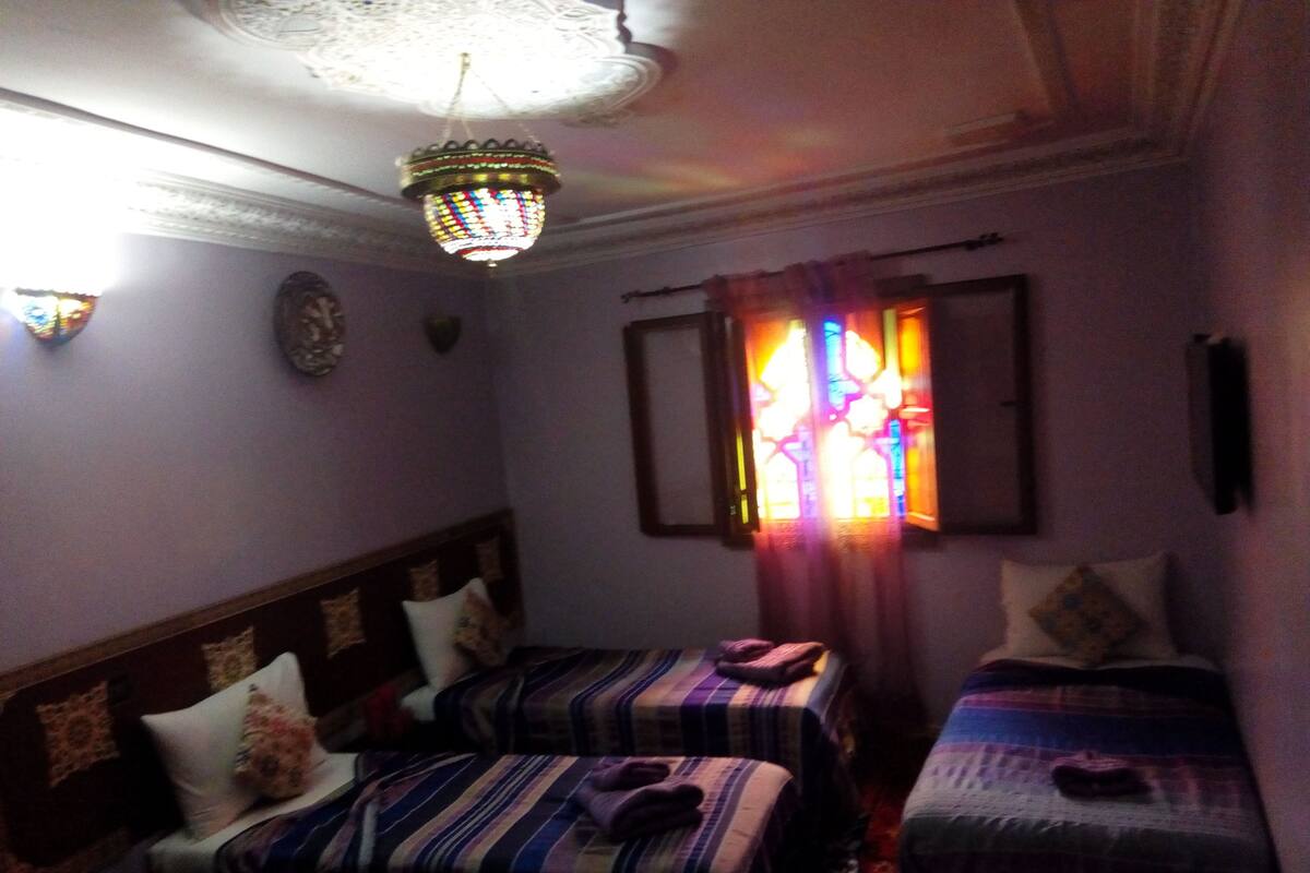 A room with two beds, a chandelier, a window with curtains, and a clock on the wall.