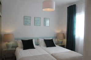 Une chambre d’hôtel avec deux lits, une grande fenêtre avec des rideaux et des œuvres d’art accrochées au mur.