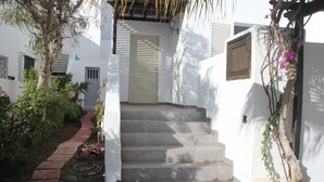 A white building with a set of stone steps leading to a door, surrounded by greenery and a brick path. - Spacious two bedroom house near the beach with private terrace and sea views (Puerto del Carmen)