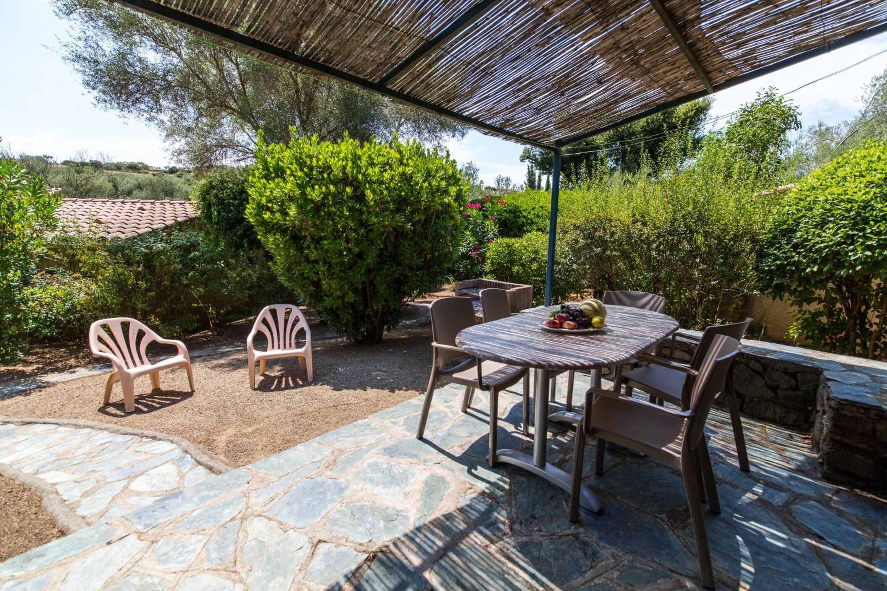 An outdoor patio with stone flooring, a round table with chairs, and a covered area with a bamboo roof.