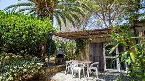 A rustic outdoor dining area with a stone wall, white plastic chairs, and a wooden table. - Residence Les Arbousiers (Oletta)