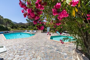 Ein Poolbereich mit Steinböden und zwei Schwimmbecken, umgeben von üppiger Vegetation und rosa Blumen.