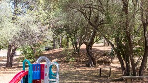 A park with a playground, including a slide and climbing structures, surrounded by trees and a picnic table. - Residence Les Arbousiers (Oletta)