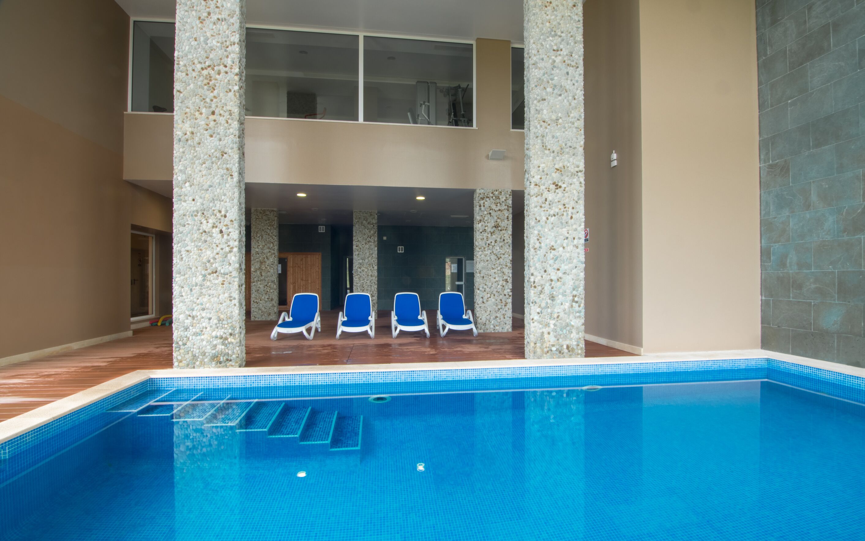 Une piscine intérieure avec des marches recouvertes de carreaux bleus menant à l’eau, entourée de murs de couleur beige et d’une colonne en pierre.