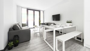 A modern, minimalist living room with a grey sofa, a white dining table, and a large window. - Destiny Student - New Mill (Dublin)