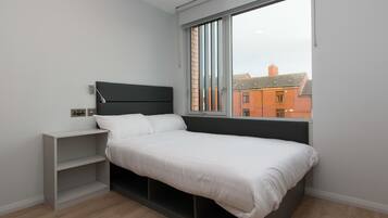 A modern bedroom with a bed, a nightstand, and a window with a view of buildings.