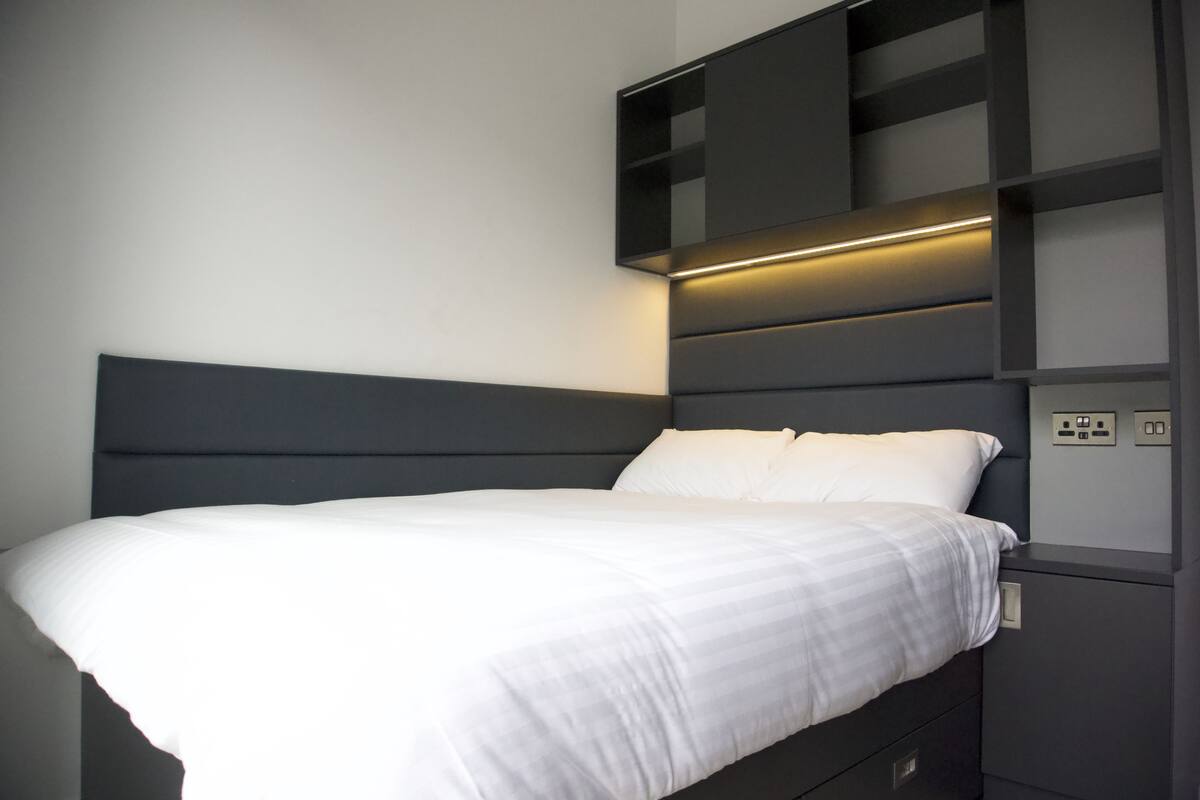 A modern bedroom with a bed, built-in shelving, and a bedside table.