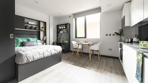A modern bedroom with a bed, bedside tables, and a desk. There is a small dining area with a table and chairs. - Destiny Student - New Mill (Dublin)