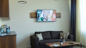 A modern living room with a dark grey sofa, a wooden coffee table, and a flat-screen TV mounted on the wall. - Motel Plus Schönefeld (Schoenefeld)
