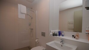 A modern bathroom with a shower, toilet, sink, and a mirror above the sink. - Motel Plus Schönefeld (Schoenefeld)