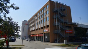 A multi-story building with a parking garage, a fire escape, and signs for a motel and a store. - Motel Plus Schönefeld (Schoenefeld)