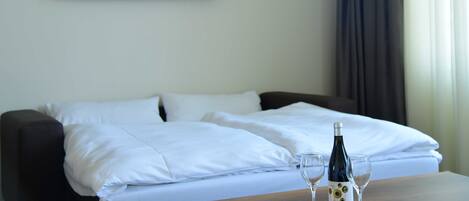 A hotel room with a bed, a TV mounted on the wall displaying a garden scene, and a table with a bottle and glasses.